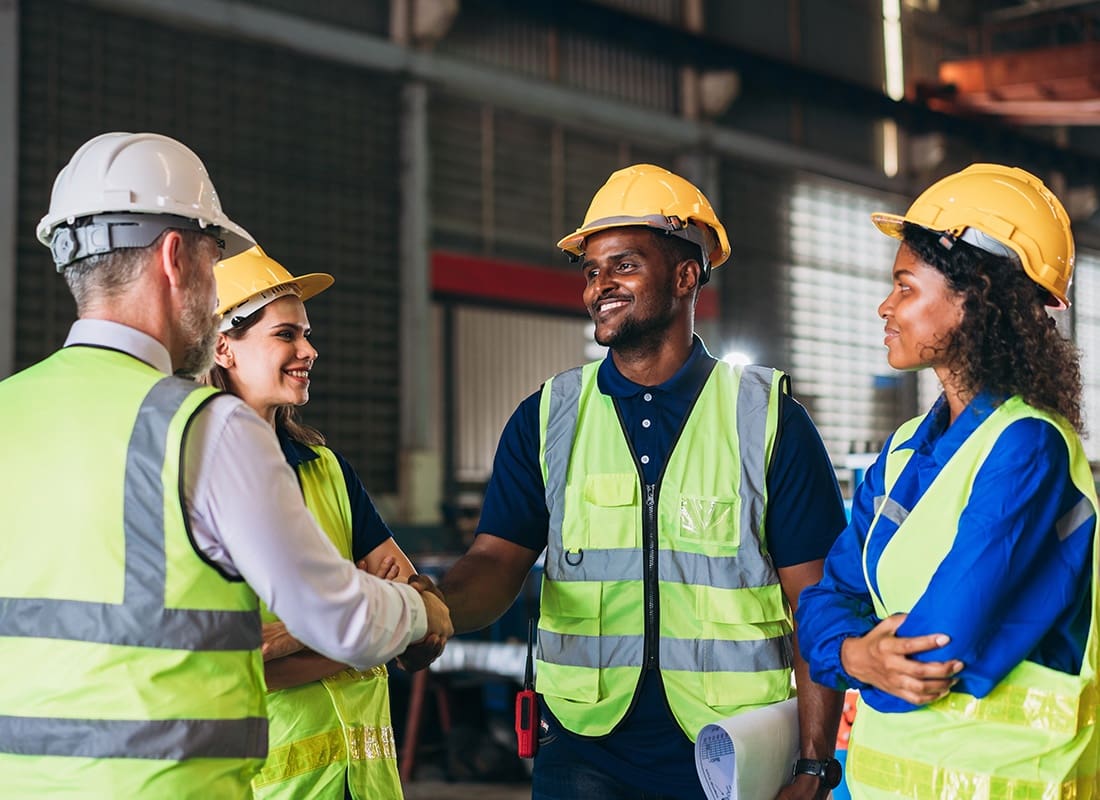 Business Insurance - Small Team of Diverse Contractors Talking During a Meeting Inside an Industrial Building with Two Contractors Shaking Hands